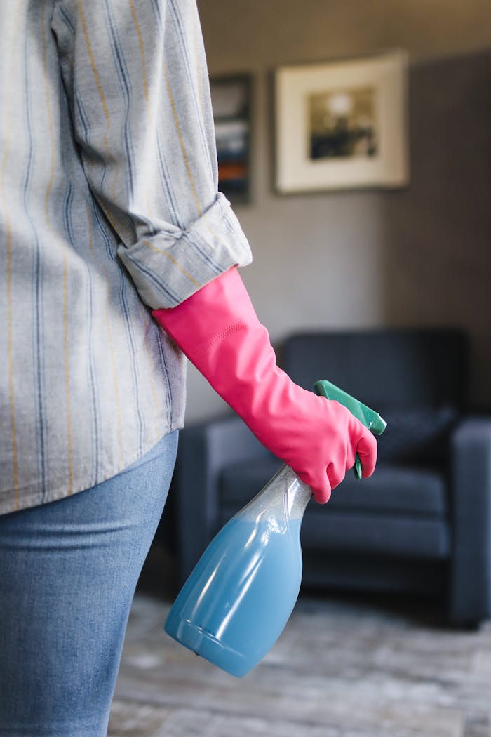 services-02 Close-up of a person in pink gloves holding a blue spray bottle indoors.